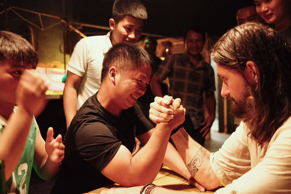 Two people engaged in a arm wrestle while onlookers cheer