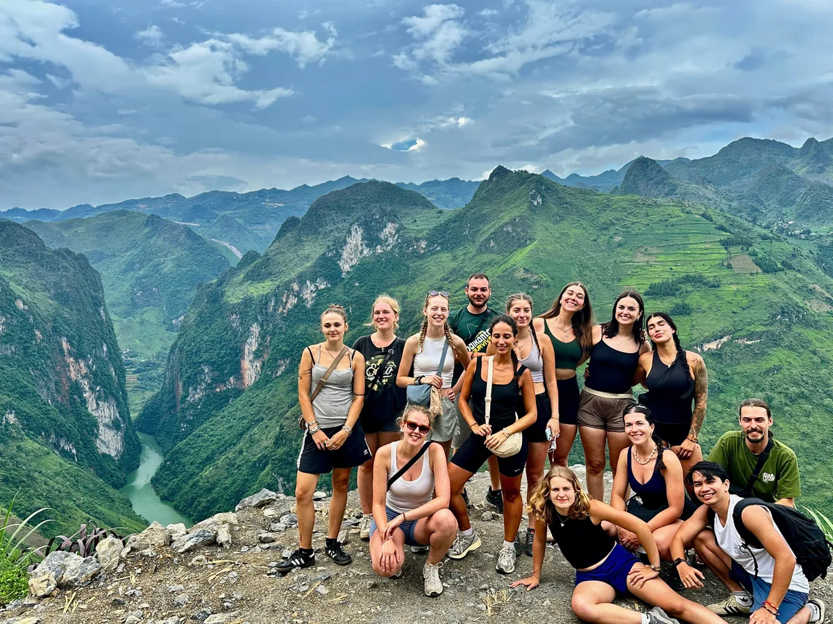 A group of people pose on the Ma Pi Leng Pass with the Nho Que river below