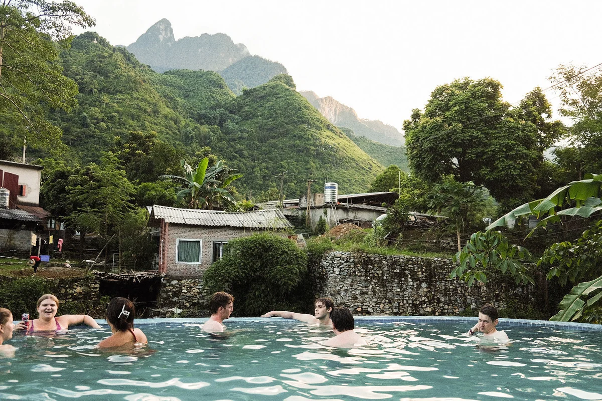A group of solo travelers get to know each other in a pool with mountains and trees behind