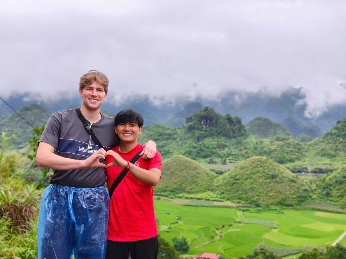 Two people pose together in front of two small mountains