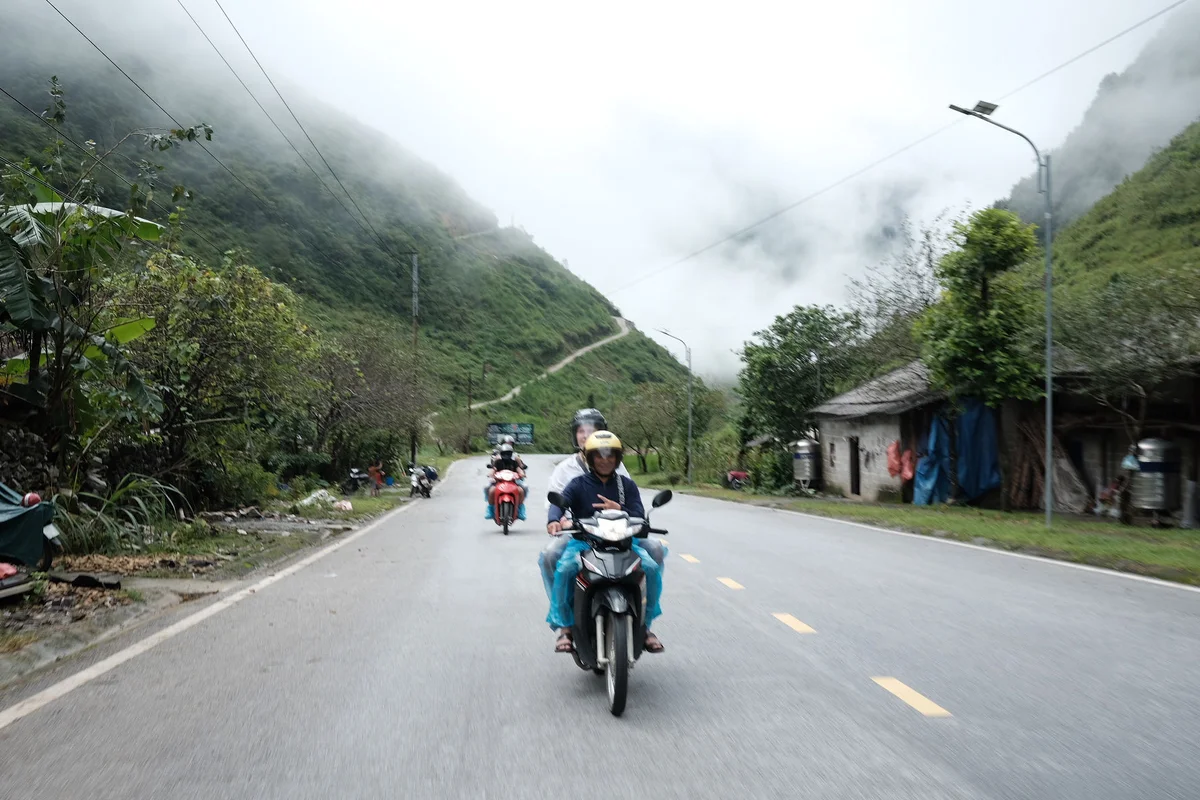 Driver makes the peace sign on the Ha Giang Loop road with mountains behind
