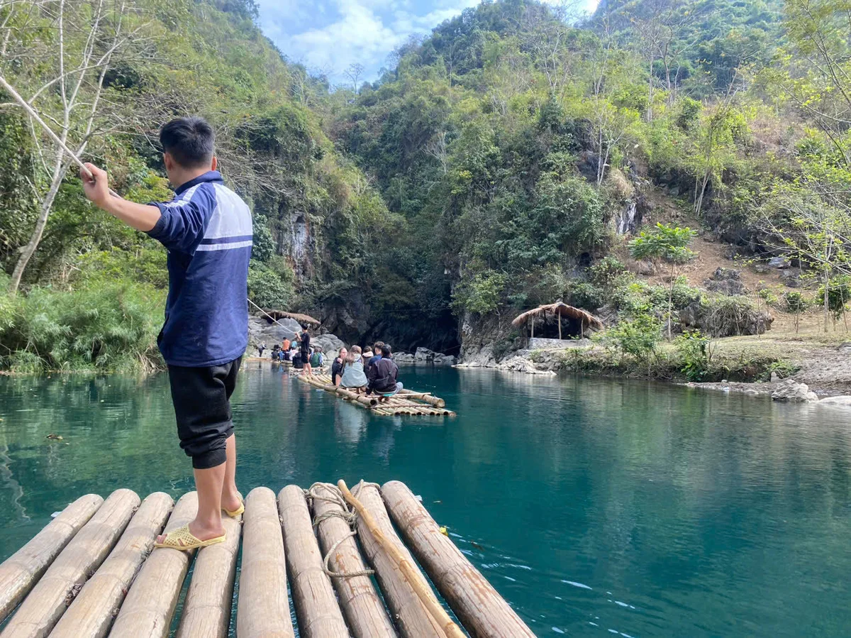 Man pulls bamboo boat down a river using a rope