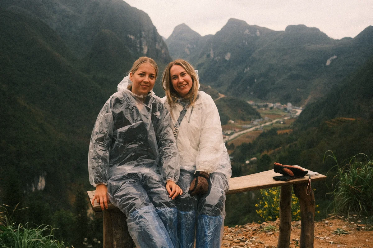 Two girls wearing ponchos pose against a mountain backdrop