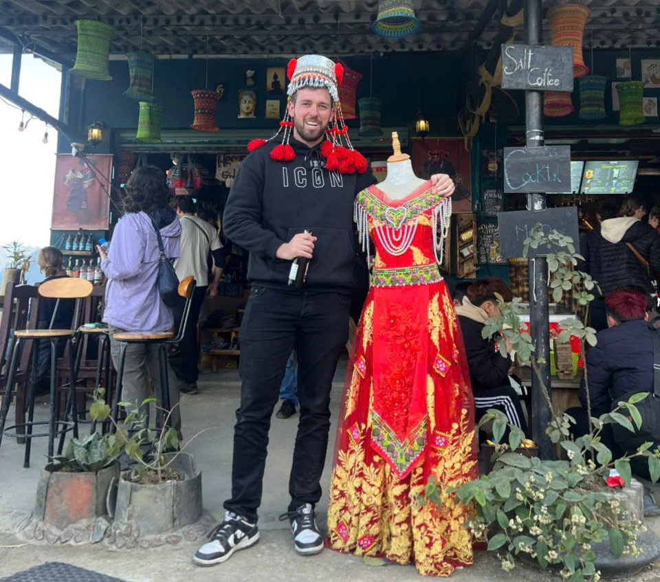Man poses with a mannequin that is dressed in traditional colors and fabrics 