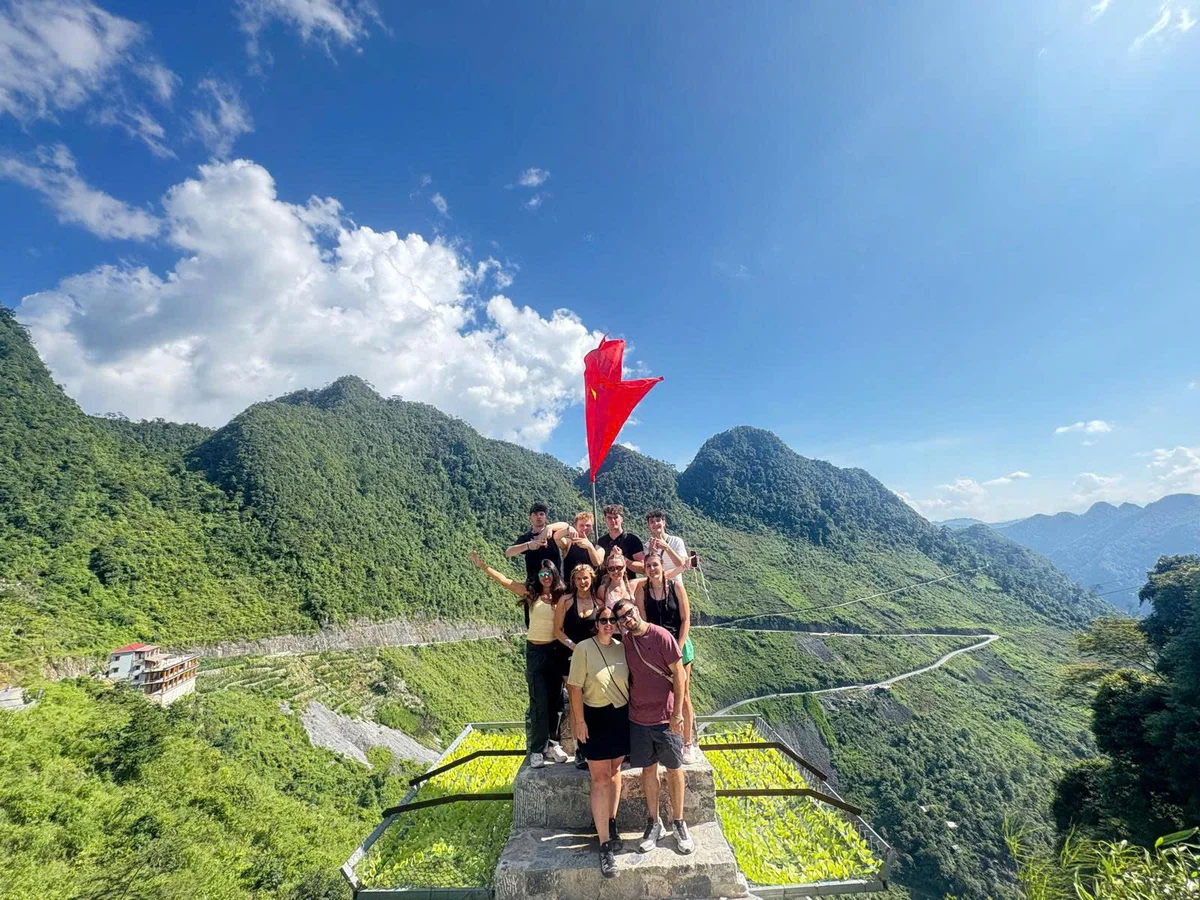 Group of people pose overlooking a green valley and winding road
