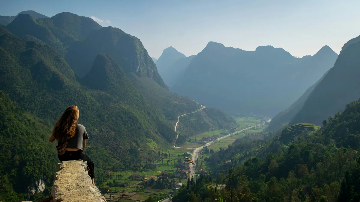 Woman gazing out over mountains and a valley below with winding roads running through it