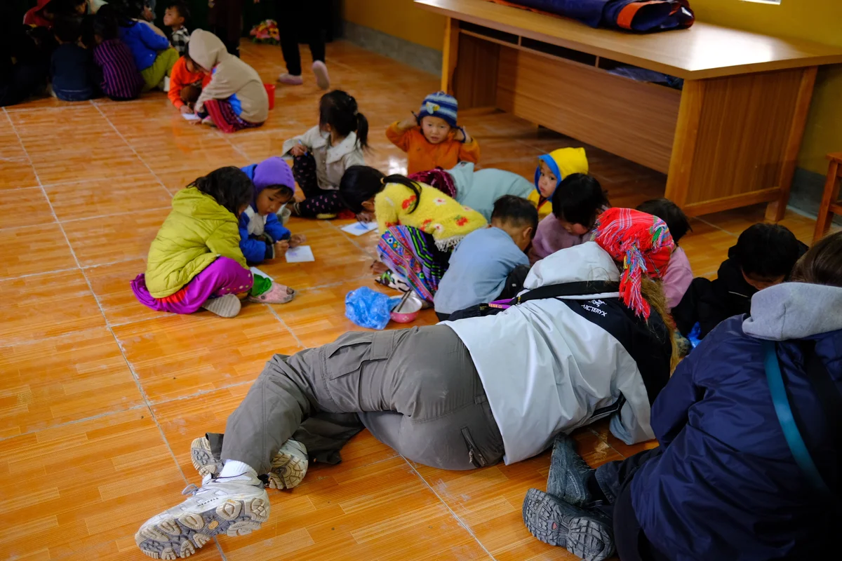 Children and a woman lie on the floor in colourful clothing drawing